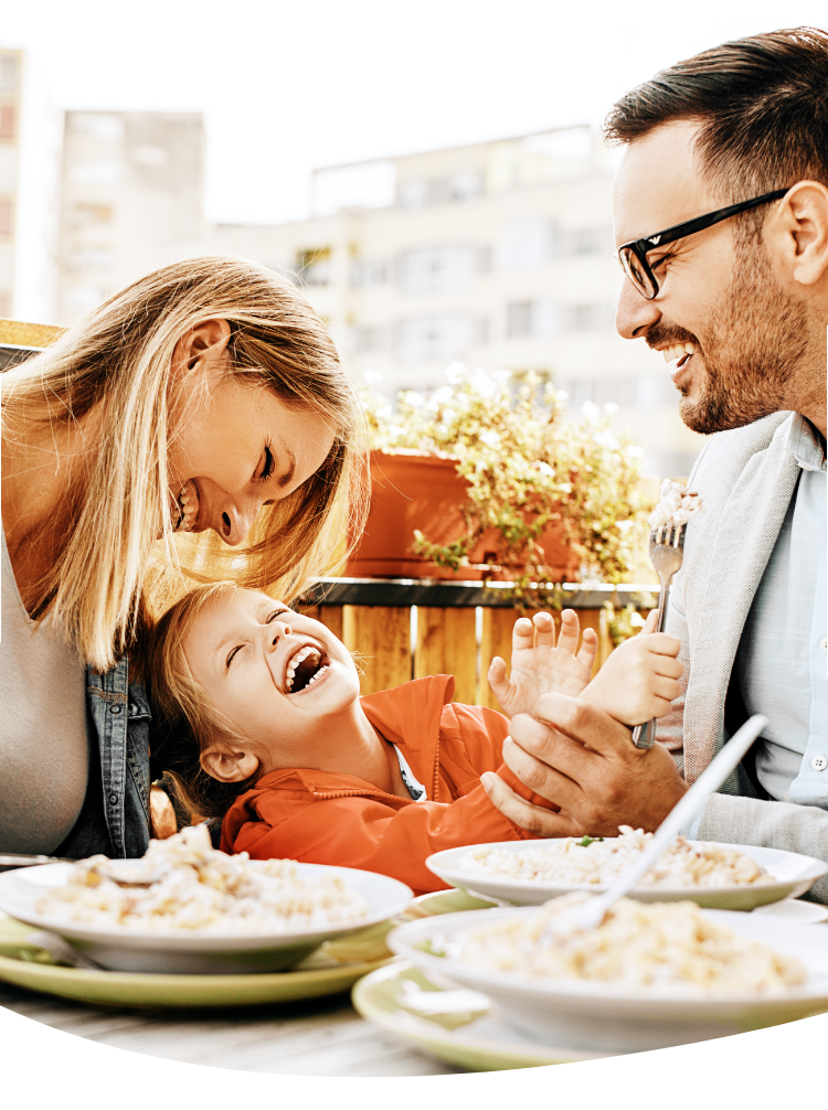 Young parents having a meal at the dining table, wearing their work clothes with their child sitting between them. They are laughing and having a good time together