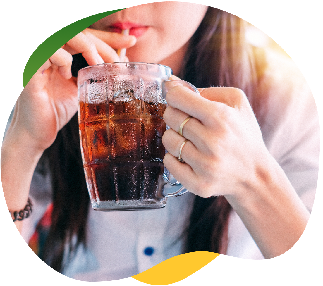 A young woman with long, brown hair holds a tall glass with her hand and drinks a carbonated drink with a straw out of it